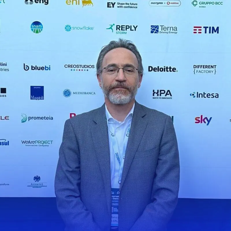 Stefano Di Persio AI Market Product Manager, sullo sfondo il pannell con le aziende partecipanti all'evento.